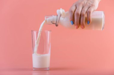 Bir kadın eli pembe bir arka plan üzerine bir bardak içine bir cam şişe taze süt dökülen. Renkli minimalizm. Kalsiyum sağlıklı süt ürünleri kavramı
