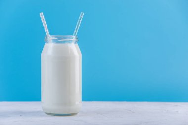 Cam şişe mavi zemin üzerine iki payet ile taze süt. Renkli minimalizm. Kalsiyum sağlıklı süt ürünleri kavramı