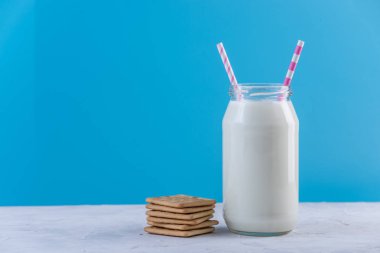 Cam şişe saman ve çerezler üzerinde mavi arka plan ile taze süt. Renkli minimalizm. Kalsiyum sağlıklı süt ürünleri kavramı