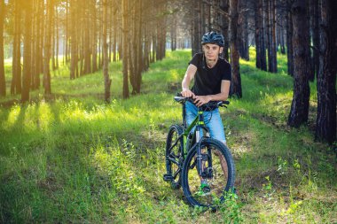 Ormanda ağaçların arasında bir yeşil dağ bisikleti binme bir kask bisikletçi adam. Etkin ve sağlıklı yaşam kavramı