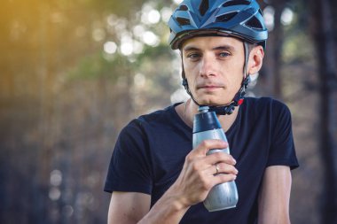 Bir bisikletçi bir kask içme suyu parkta ağaçların arasında sürme sırasında bir şişe. Etkin ve sağlıklı yaşam kavramı