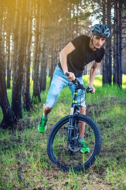 Ormanda ağaçların arasında bir yeşil dağ bisikleti binme bir kask içinde bir adam. Bisikletçi hareket. Etkin ve sağlıklı yaşam kavramı