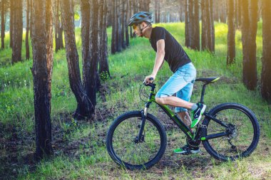 Ormanda ağaçların arasında bir yeşil dağ bisikleti binme bir kask içinde bir adam. Bisikletçi hareket. Etkin ve sağlıklı yaşam kavramı
