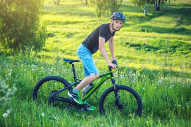 Ormanda ağaçların arasında bir yeşil dağ bisikleti binme bir kask içinde bir adam. Bisikletçi hareket. Etkin ve sağlıklı yaşam kavramı