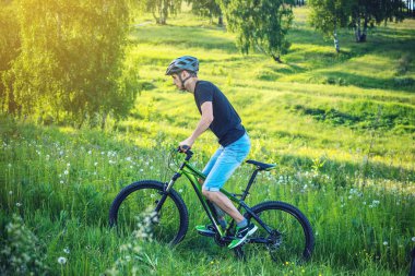 Ormanda ağaçların arasında bir yeşil dağ bisikleti binme bir kask içinde bir adam. Bisikletçi hareket. Etkin ve sağlıklı yaşam kavramı