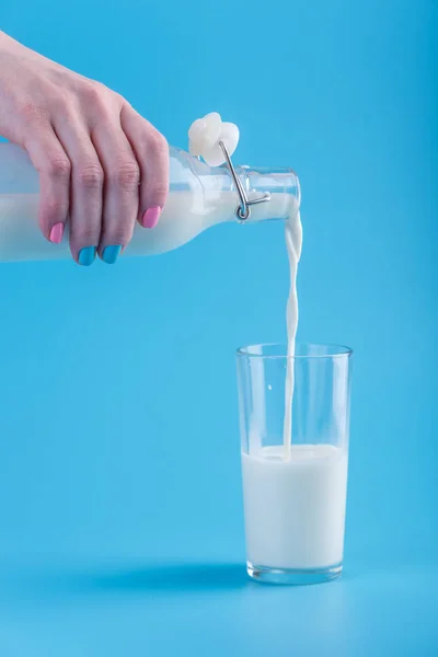 Woman Hand Pours Fresh Milk Glass Bottle Glass Blue Background — Stock Photo, Image