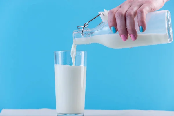 Woman Hand Pours Fresh Milk Glass Bottle Glass Blue Background — Stock Photo, Image