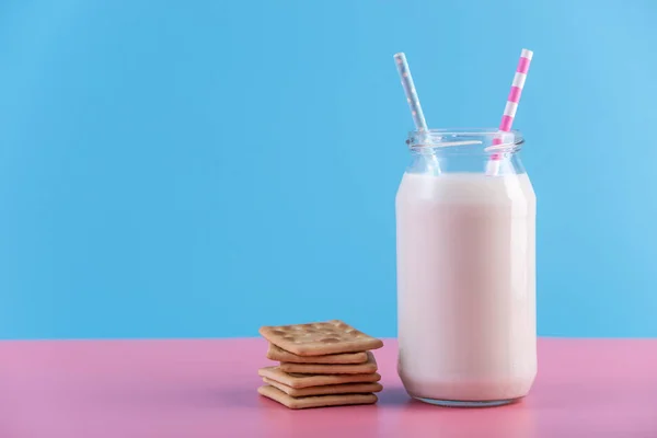 つのストローとパステル調の背景にクッキーとミルクのガラス瓶 カラフルなミニマリズム カルシウムと健康的な乳製品の概念 — ストック写真