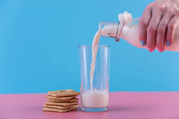 一个女人的手把新鲜的牛奶从玻璃瓶倒入玻璃和饼干的柔和背景 多彩简约 健康乳制品与钙的概念 — 图库照片