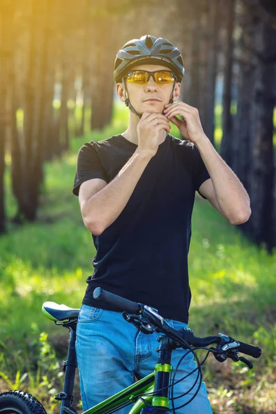 Adam bisikletçi başını yeşil doğa arka planda gri spor kask giyiyor. Bisiklete binme sırasında zorunlu koruma kavramı