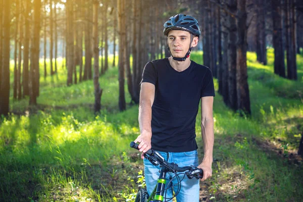 Ormanda ağaçların arasında bir yeşil dağ bisikleti binme bir kask bisikletçi adam. Etkin ve sağlıklı yaşam kavramı