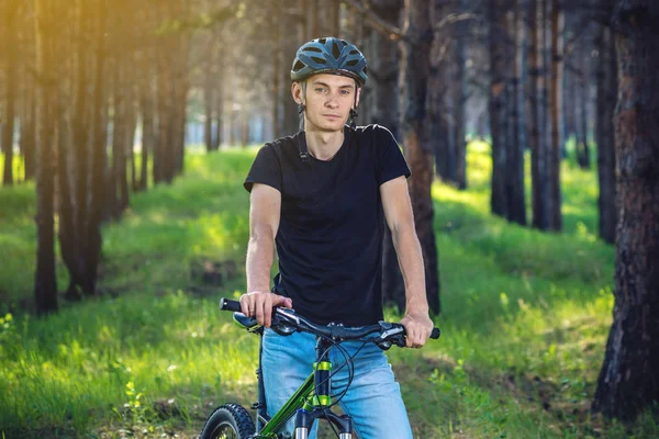 Ormanda ağaçların arasında bir yeşil dağ bisikleti binme bir kask bisikletçi adam. Etkin ve sağlıklı yaşam kavramı