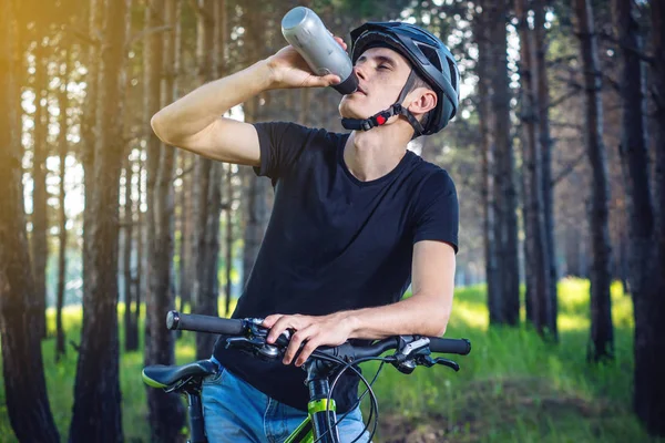 Bir bisikletçi bir kask içme suyu parkta ağaçların arasında sürme sırasında bir şişe. Etkin ve sağlıklı yaşam kavramı