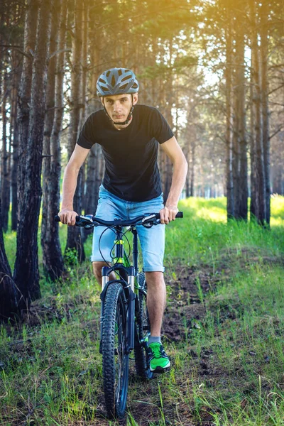 Ormanda ağaçların arasında bir yeşil dağ bisikleti binme bir kask içinde bir adam. Bisikletçi hareket. Etkin ve sağlıklı yaşam kavramı