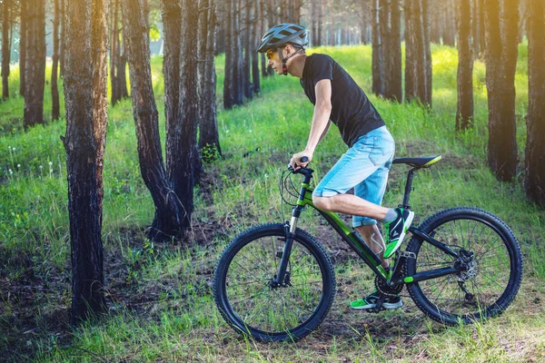 Ormanda ağaçların arasında bir yeşil dağ bisikleti binme bir kask içinde bir adam. Bisikletçi hareket. Etkin ve sağlıklı yaşam kavramı