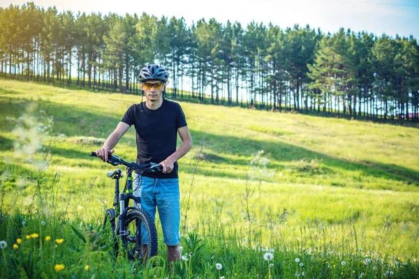 Ormanda ağaçların arasında bir yeşil dağ bisikleti binme bir kask bisikletçi adam. Etkin ve sağlıklı yaşam kavramı