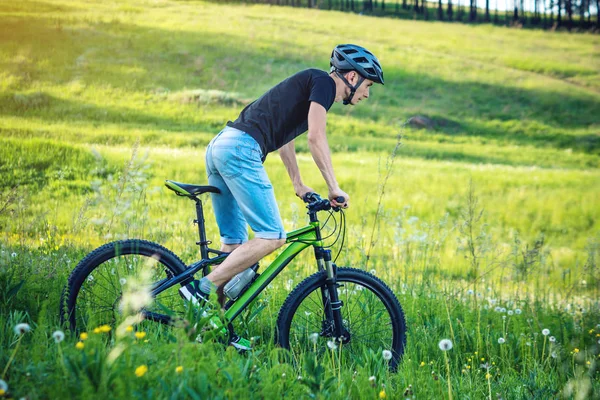 Ormanda ağaçların arasında bir yeşil dağ bisikleti binme bir kask içinde bir adam. Bisikletçi hareket. Etkin ve sağlıklı yaşam kavramı
