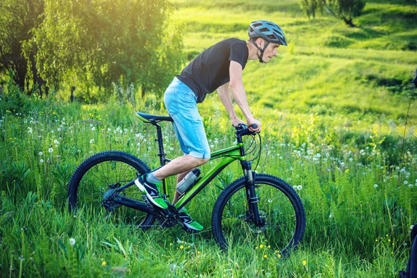 Ormanda ağaçların arasında bir yeşil dağ bisikleti binme bir kask içinde bir adam. Bisikletçi hareket. Etkin ve sağlıklı yaşam kavramı