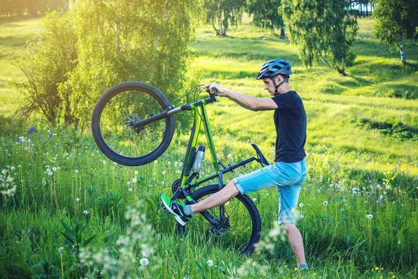 Ormanda ağaçların arasında bir yeşil dağ bisikleti binme bir kask içinde bir adam. Bisikletçi hareket. Etkin ve sağlıklı yaşam kavramı