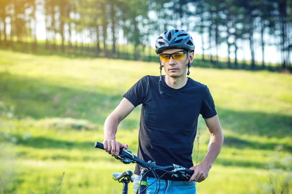 Ormanda ağaçların arasında bir yeşil dağ bisikleti binme bir kask bisikletçi adam. Etkin ve sağlıklı yaşam kavramı