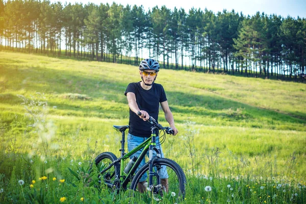 Ormanda ağaçların arasında bir yeşil dağ bisikleti binme bir kask bisikletçi adam. Etkin ve sağlıklı yaşam kavramı