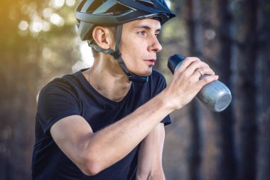 Bir bisikletçi bir kask içme suyu parkta ağaçların arasında sürme sırasında bir şişe. Etkin ve sağlıklı yaşam kavramı
