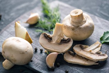 Taze beyaz Şampiyonlar, yeşil dereotu ve malzemelerin karanlık mutfak masasının üzerine. Mantar yemekleri pişirme kavramı. Yakın çekim