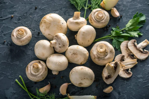 Taze beyaz Şampiyonlar, yeşil dereotu ve malzemelerin karanlık mutfak masasının üzerine. Mantar yemekleri pişirme kavramı