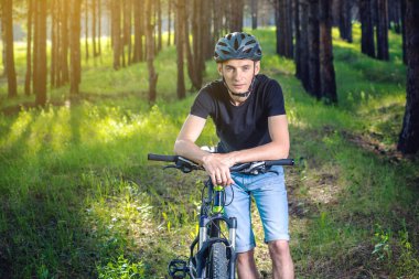 Ormanda ağaçların arasında bir yeşil dağ bisikleti binme bir kask bisikletçi adam. Etkin ve sağlıklı yaşam kavramı