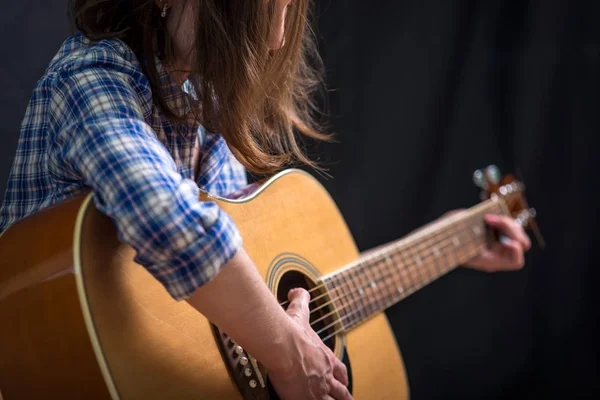 那个十几岁的少女在录音室的黑暗背景下弹奏一把声学吉他 音乐会年轻音乐家 — 图库照片