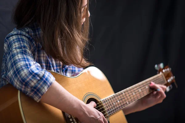 那个十几岁的少女在录音室的黑暗背景下弹奏一把声学吉他 音乐会年轻音乐家 — 图库照片
