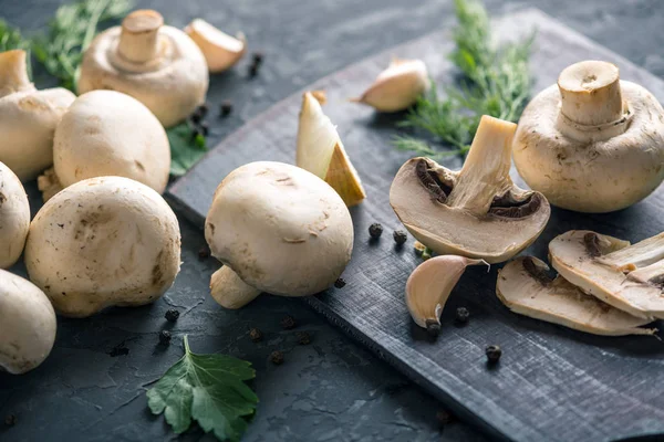 Fresh white Champions, green dill and ingredients on the dark kitchen table. The concept of cooking mushroom dishes. Close up