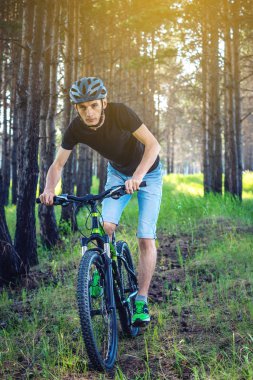 Ormanda ağaçların arasında bir yeşil dağ bisikleti binme bir kask içinde bir adam. Bisikletçi hareket. Etkin ve sağlıklı yaşam kavramı