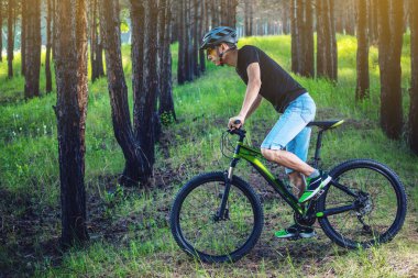 Ormanda ağaçların arasında bir yeşil dağ bisikleti binme bir kask içinde bir adam. Bisikletçi hareket. Etkin ve sağlıklı yaşam kavramı