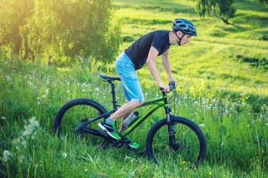 Ormanda ağaçların arasında bir yeşil dağ bisikleti binme bir kask içinde bir adam. Bisikletçi hareket. Etkin ve sağlıklı yaşam kavramı