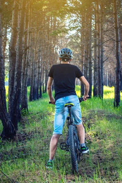 Ormanda ağaçların arasında bir yeşil dağ bisikleti binme bir kask içinde bir adam. Arkadan görünüm. Etkin ve sağlıklı yaşam kavramı