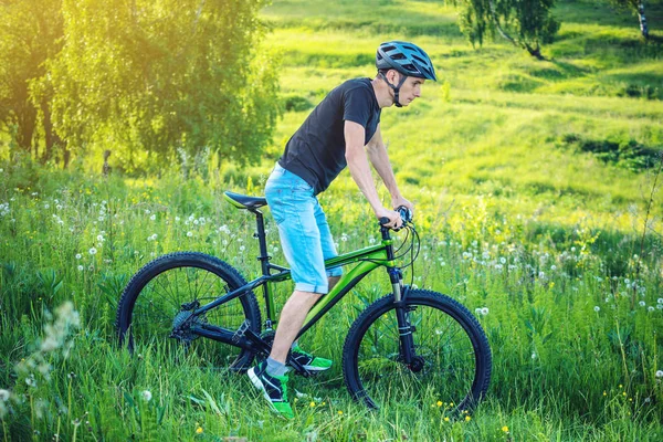 Ormanda ağaçların arasında bir yeşil dağ bisikleti binme bir kask içinde bir adam. Bisikletçi hareket. Etkin ve sağlıklı yaşam kavramı