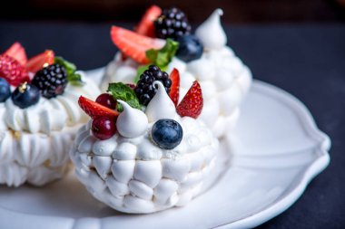 Hassas beyaz meringues plaka üzerinde taze çilek ile. Tatlı Pavlova yakın çekim. Koyu arka plan. Şenlikli bir düğün pastası.