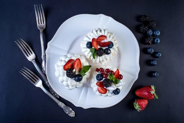 Hassas beyaz meringues plaka üzerinde taze çilek ile. Tatlı Pavlova yakın çekim. Koyu arka plan. Şenlikli bir düğün pastası.