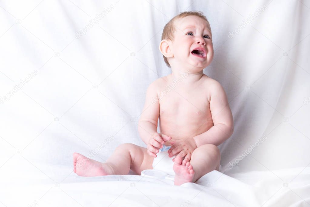 Cute blue-eyed baby 6-9 months old sad crying white background. Children's emotions. The pain of teething