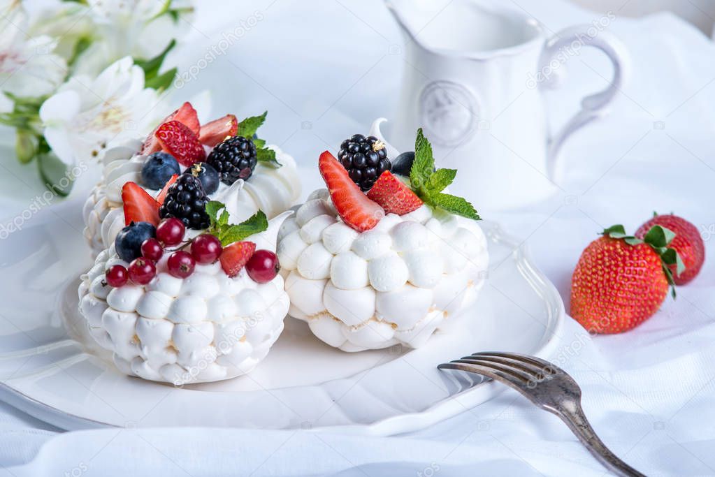 Delicate white meringues with fresh berries on the plate. Dessert Pavlova close-up. White background. A festive wedding cake.