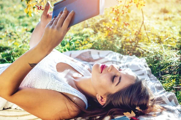 秋の日 サニーに緑の芝生の公園で横になっている面白い本を読んで魅力的な女性 学生教育の概念 — ストック写真