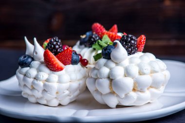 Hassas beyaz meringues plaka üzerinde taze çilek ile. Tatlı Pavlova yakın çekim. Koyu arka plan. Şenlikli bir düğün pastası.