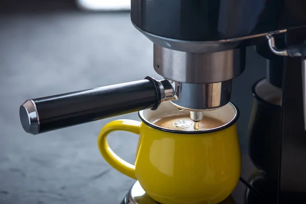 Preparation of espresso. Black coffee pouring from the machine into the Yellow Cup. Professional coffee brewing at home
