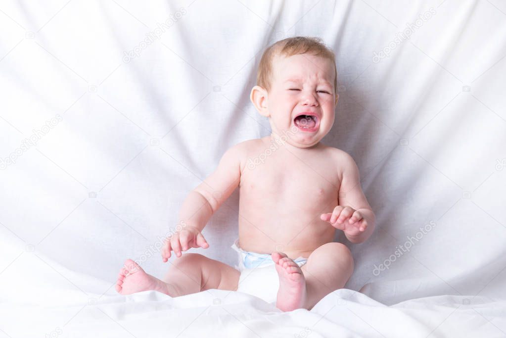 Cute blue-eyed baby 6-9 months old sad crying white background. Children's emotions. The pain of teething