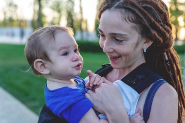 Genç mutlu anne bebek oğlu ile ergo sırt çantası Park'ta yürüyordunuz. Güneşli yaz günü. Modern anne kavramı