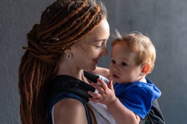 Genç mutlu anne bebek oğlu ile ergo sırt çantası Park'ta yürüyordunuz. Güneşli yaz günü. Modern anne kavramı