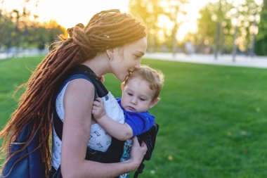 Genç Anne Bebek oğlu ile ergo sırt çantası mutlu parkta oynuyorlar. Güneşli yaz günü. Modern anne kavramı