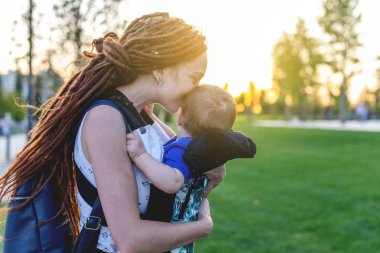 Genç Anne Bebek oğlu ile ergo sırt çantası mutlu parkta oynuyorlar. Güneşli yaz günü. Modern anne kavramı