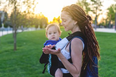 Genç mutlu anne bebek oğlu ile ergo birlikte seyahat etmek sırt çantası. Güneşli yaz günü. Modern anne kavramı